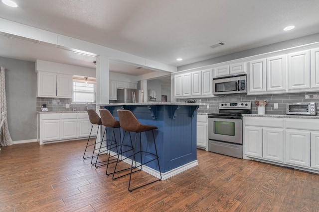 4100 Skyline Dr, Midland, TX 79707 - kitchen with appliances with stainless steel finishes, a breakfast bar, backsplash, dark wood finished floors, and white cabinets