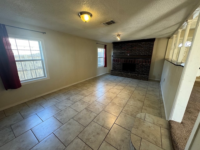 unfurnished room featuring a textured ceiling, a brick fireplace, and a wealth of natural light