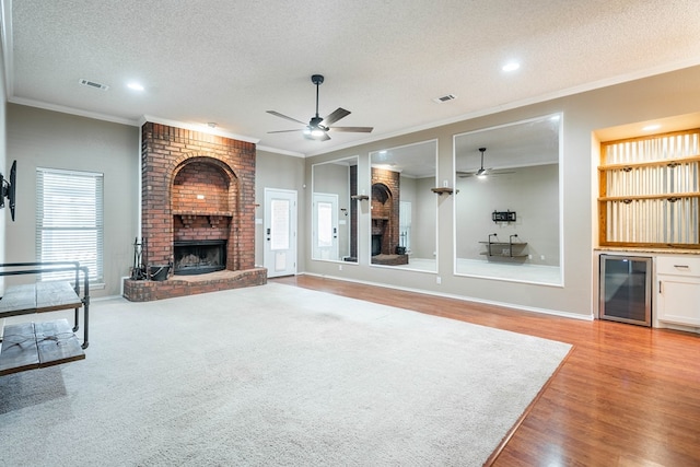 unfurnished living room with wine cooler, a brick fireplace, crown molding, and a textured ceiling