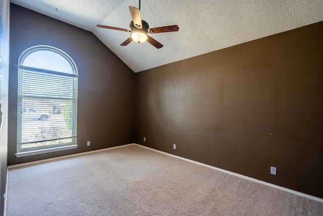 empty room featuring a textured ceiling, carpet floors, a ceiling fan, baseboards, and vaulted ceiling