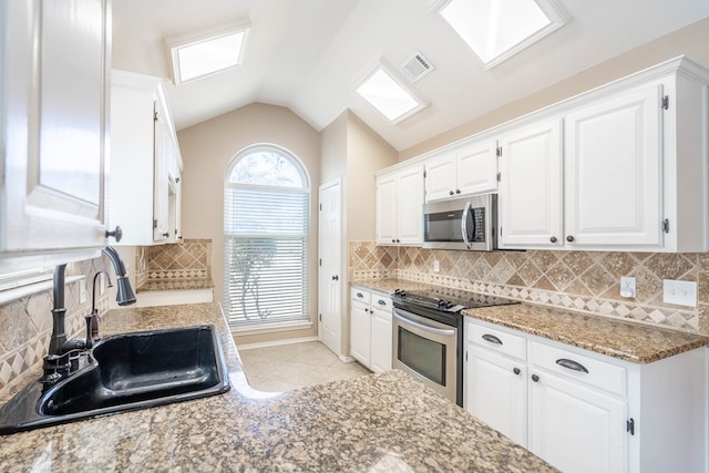 kitchen featuring lofted ceiling, visible vents, appliances with stainless steel finishes, white cabinetry, and a sink