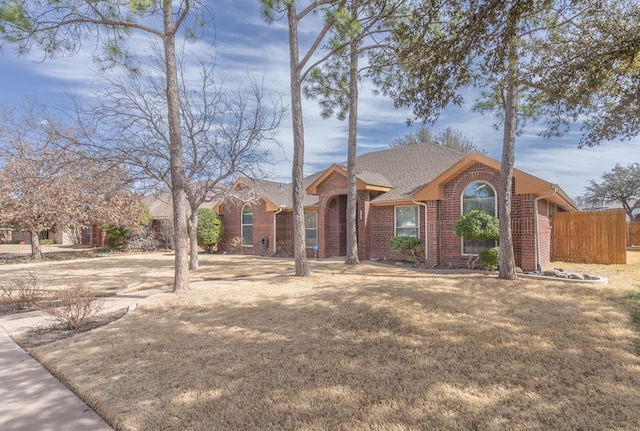 view of front of house featuring brick siding, roof with shingles, a front yard, and fence