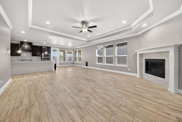 1803 Overshine Ln, Midland, TX 79705 - unfurnished living room featuring a raised ceiling, a ceiling fan, light wood-style floors, crown molding, and a fireplace