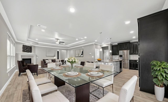 1803 Overshine Ln, Midland, TX 79705 - dining space featuring a ceiling fan, crown molding, a tray ceiling, light wood finished floors, and a glass covered fireplace
