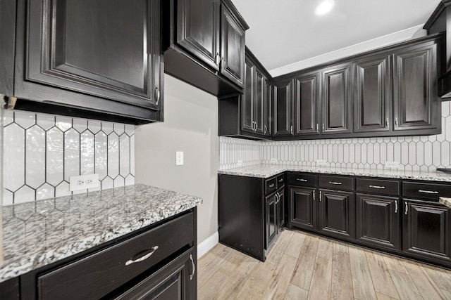 1803 Overshine Ln, Midland, TX 79705 - kitchen featuring decorative backsplash, light stone counters, light wood-style flooring, and dark cabinets