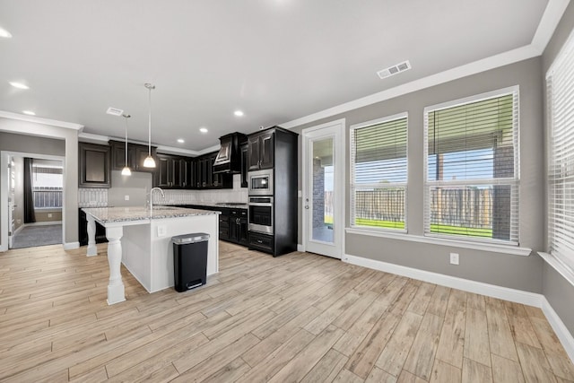 1803 Overshine Ln, Midland, TX 79705 - kitchen with appliances with stainless steel finishes, light wood-type flooring, custom range hood, a kitchen island with sink, and tasteful backsplash
