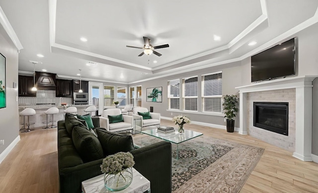 1803 Overshine Ln, Midland, TX 79705 - living room featuring a raised ceiling, a ceiling fan, light wood-style flooring, a glass covered fireplace, and crown molding