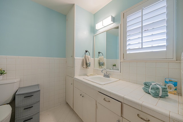 bathroom featuring vanity, a wainscoted wall, toilet, and tile walls
