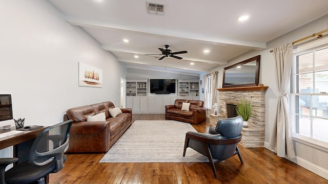 living room featuring ceiling fan, visible vents, a fireplace, wood finished floors, and vaulted ceiling with beams