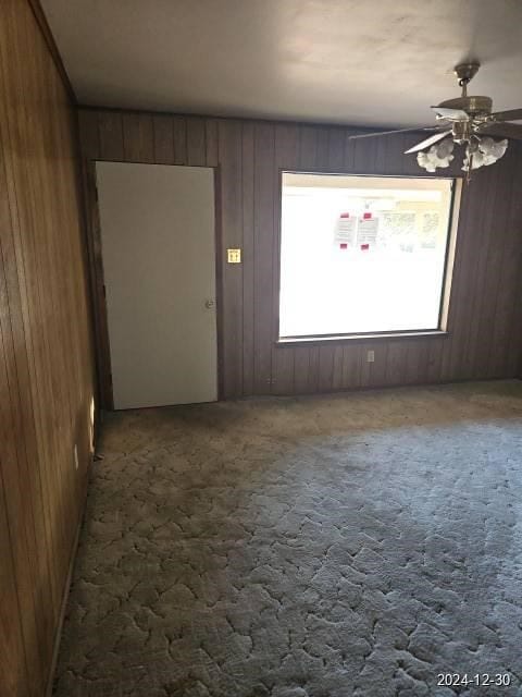 spare room featuring carpet floors, ceiling fan, and wooden walls