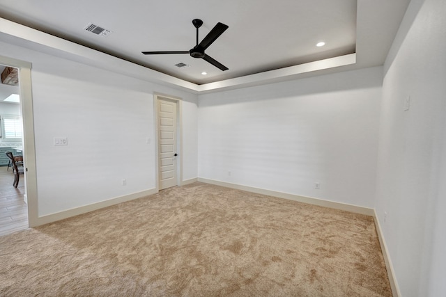 unfurnished room featuring ceiling fan, light colored carpet, and a raised ceiling