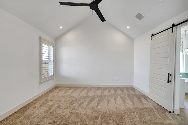 empty room featuring ceiling fan, light colored carpet, a barn door, and vaulted ceiling