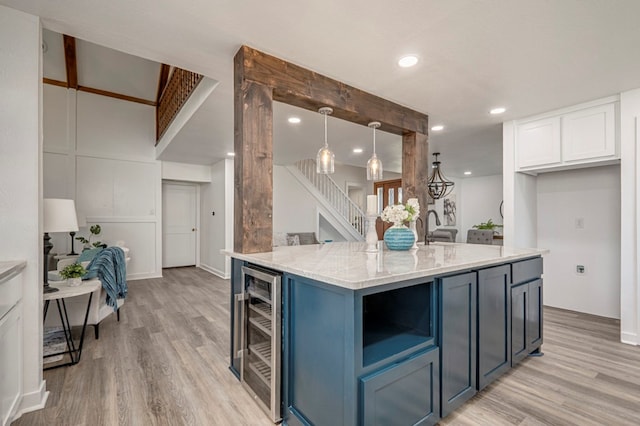 kitchen with light stone countertops, wine cooler, light wood-type flooring, white cabinetry, and blue cabinets