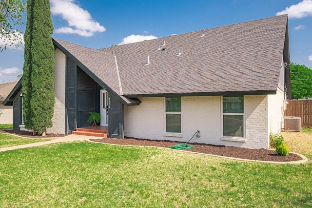 view of front facade featuring roof with shingles, a front lawn, central air condition unit, and brick siding