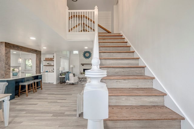 stairs featuring recessed lighting, wood finished floors, and a high ceiling