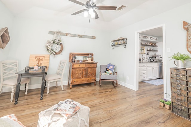 living area with a raised ceiling, ceiling fan, sink, and light wood-type flooring