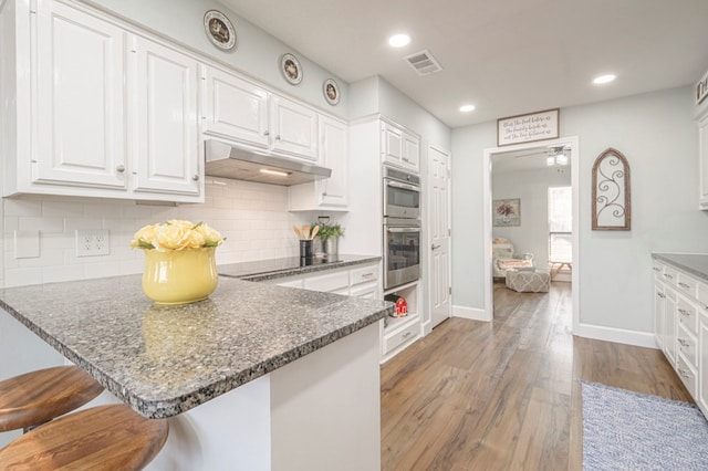 kitchen featuring a breakfast bar area, black electric stovetop, hardwood / wood-style floors, decorative backsplash, and white cabinets