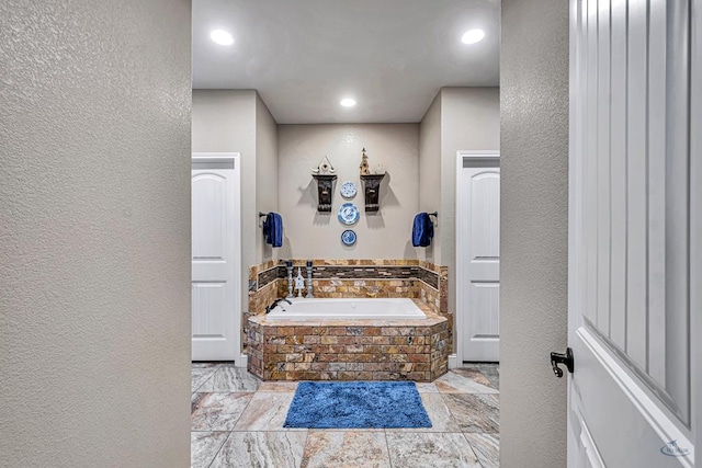 1210 S County Rd 1117, Midland, TX 79706 - bathroom with a bath, a textured wall, stone tile flooring, and recessed lighting