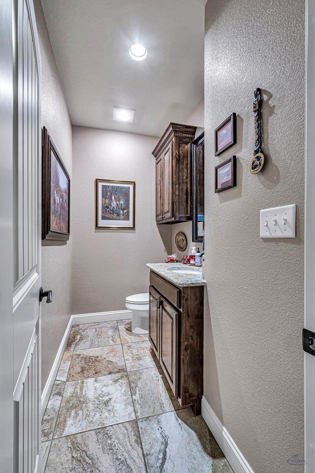1210 S County Rd 1117, Midland, TX 79706 - bathroom featuring vanity, toilet, baseboards, a textured wall, and stone tile flooring