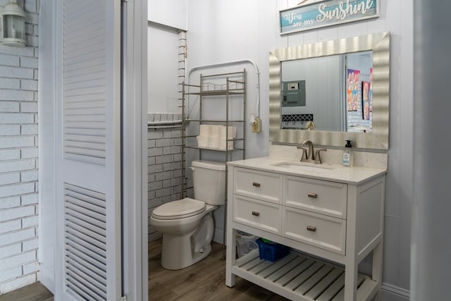 bathroom with wood-type flooring, brick wall, vanity, and toilet