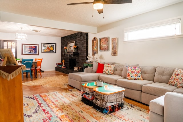 tiled living room with ceiling fan, a brick fireplace, and a textured ceiling