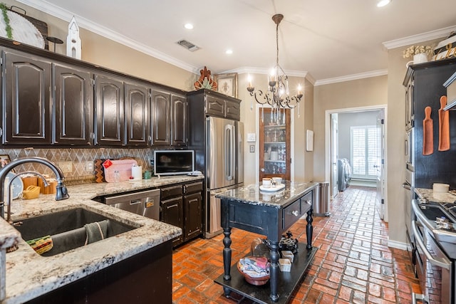 kitchen with stainless steel appliances, light stone counters, backsplash, crown molding, and decorative light fixtures