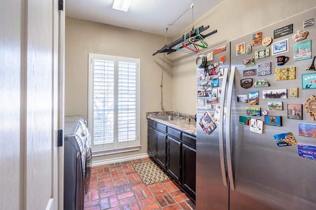 kitchen featuring light stone countertops, sink, stainless steel refrigerator, and washing machine and clothes dryer