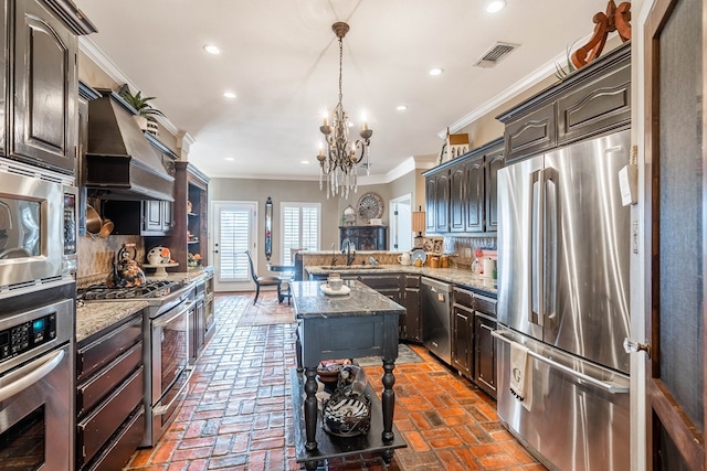 kitchen featuring appliances with stainless steel finishes, ornamental molding, a chandelier, a center island, and hanging light fixtures