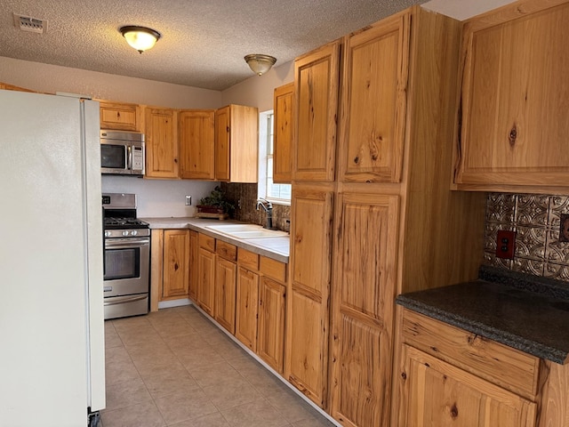 kitchen with sink, light tile patterned floors, a textured ceiling, and appliances with stainless steel finishes