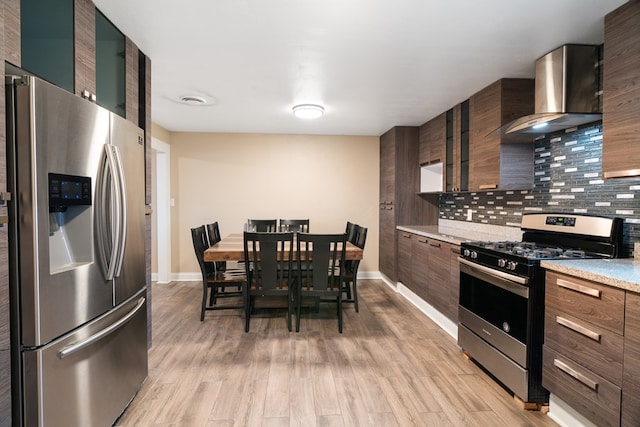 kitchen featuring backsplash, wall chimney range hood, light hardwood / wood-style floors, dark brown cabinetry, and stainless steel appliances