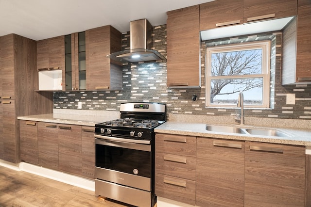 kitchen with light stone countertops, stainless steel gas stove, wall chimney exhaust hood, sink, and tasteful backsplash