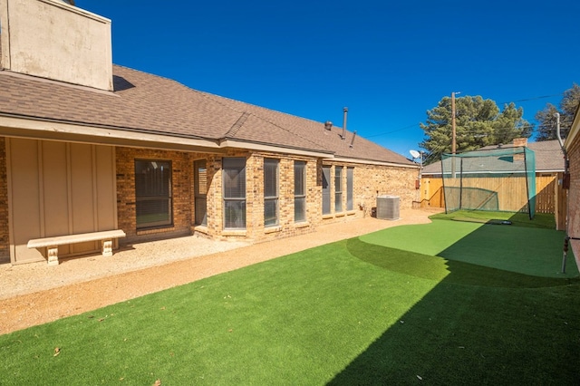 back of property featuring an outbuilding, roof with shingles, brick siding, central AC unit, and fence