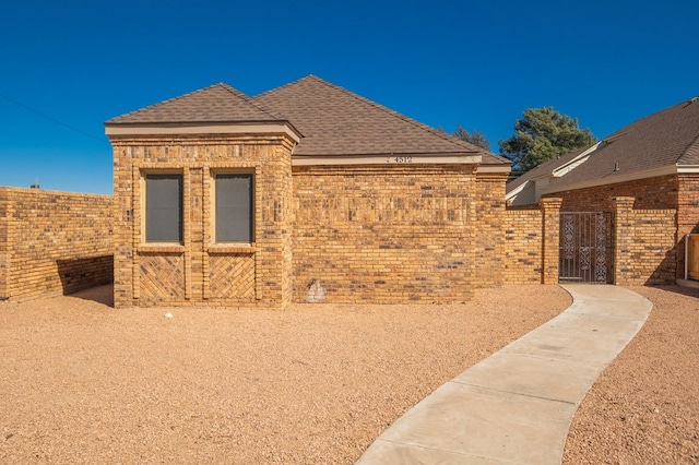 view of property exterior featuring a shingled roof, brick siding, and fence