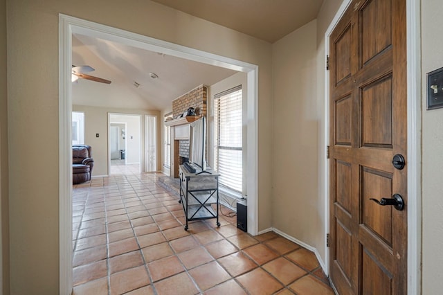 entryway with light tile patterned floors, a fireplace, lofted ceiling, and baseboards