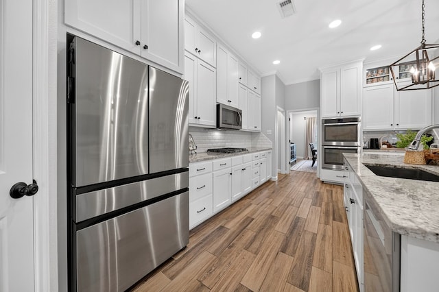 6113 Turtle Creek Rd, Midland, TX 79707 - kitchen with appliances with stainless steel finishes, a chandelier, ornamental molding, white cabinetry, and decorative backsplash