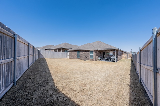 rear view of house with brick siding, roof with shingles, a fenced backyard, and a lawn