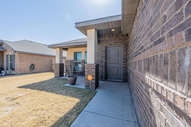 property entrance with stucco siding, brick siding, a yard, and a patio area