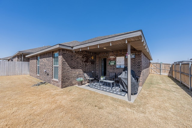 rear view of house featuring a yard, a patio, brick siding, and a fenced backyard