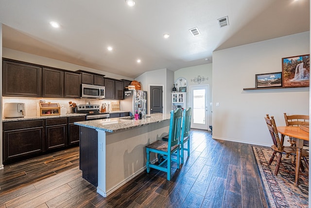 kitchen featuring visible vents, lofted ceiling, an island with sink, stainless steel appliances, and a kitchen breakfast bar