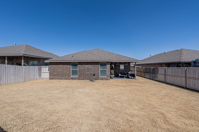 back of house featuring a yard, a fenced backyard, brick siding, and a shingled roof