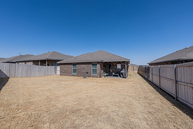 back of property with brick siding, a fenced backyard, a shingled roof, and a yard