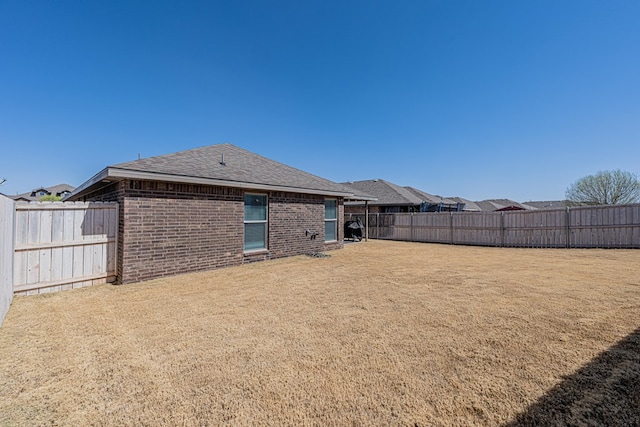 back of house featuring a fenced backyard, brick siding, and a lawn