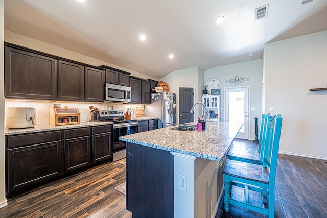 kitchen with visible vents, an island with sink, stainless steel appliances, decorative backsplash, and dark wood-type flooring