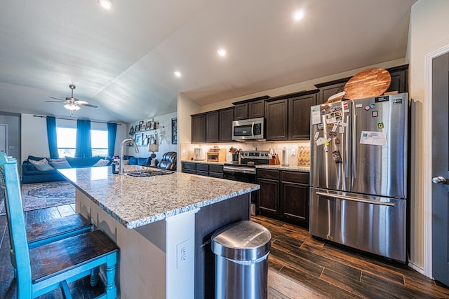 kitchen with a breakfast bar, vaulted ceiling, dark wood-style flooring, appliances with stainless steel finishes, and a kitchen island with sink