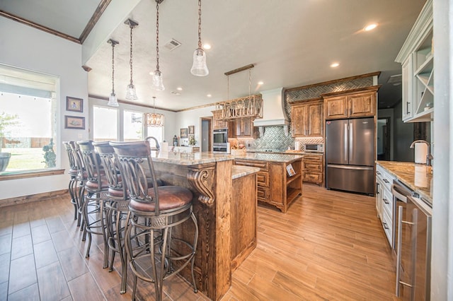 kitchen with appliances with stainless steel finishes, custom range hood, pendant lighting, a breakfast bar area, and a large island