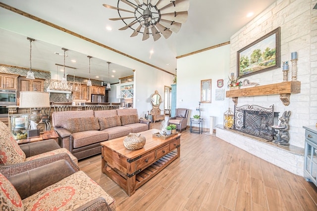 living room featuring ceiling fan, a stone fireplace, crown molding, and light hardwood / wood-style flooring