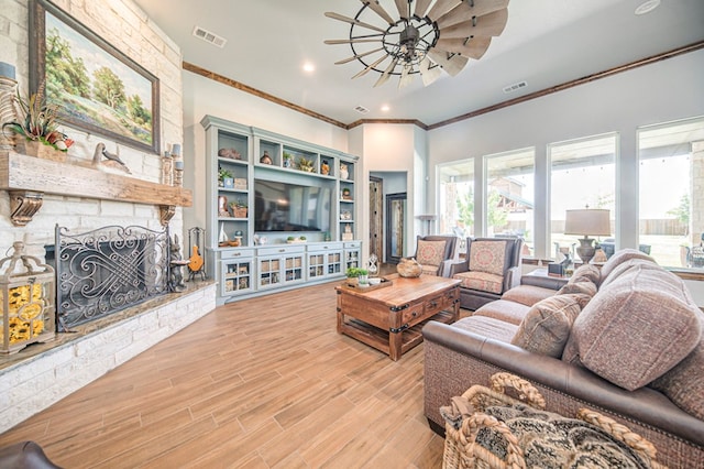 living room featuring ceiling fan, a fireplace, crown molding, and light wood-type flooring