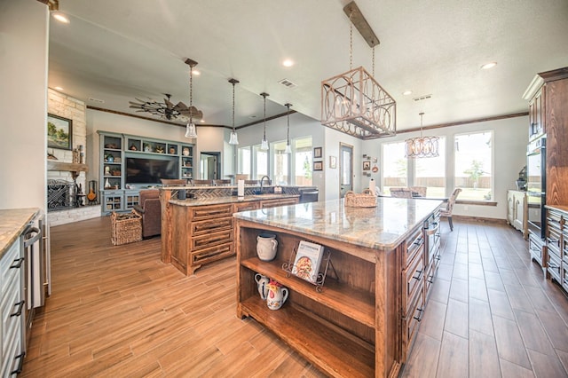 kitchen featuring light stone countertops, sink, a stone fireplace, pendant lighting, and a kitchen island