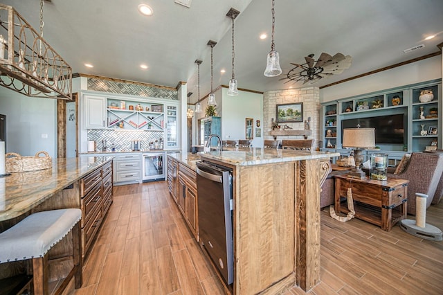 kitchen featuring a large island, light stone counters, stainless steel dishwasher, a breakfast bar area, and white cabinets