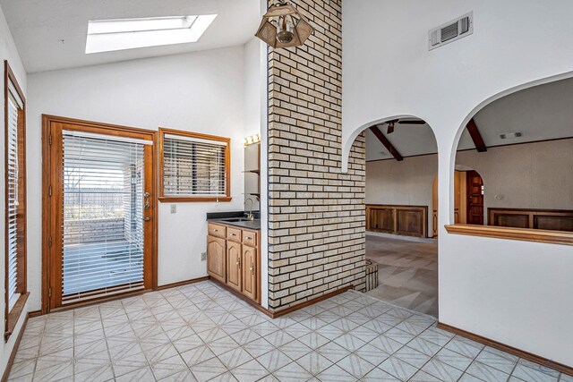 kitchen featuring visible vents, high vaulted ceiling, dark countertops, arched walkways, and a skylight